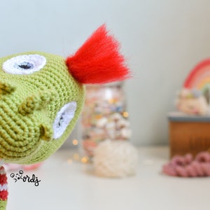 Peut inclure: Poupée verte au crochet faite à la main avec une touffe de cheveux rouge. La poupée a des yeux blancs et porte une chemise rayée rouge et blanche. Un article fantaisiste fait à la main.