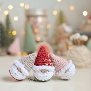 Op de afbeelding: Drie gehaakte gnomen met verschillende gekleurde mutsen. De gnome links heeft een beige muts, de middelste gnome heeft een rode muts met gouden glitter en de gnome rechts heeft een roze muts.