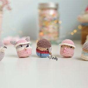 May include: Five crocheted amigurumi toys, each with a different design and color. The toys are made of yarn and have small, embroidered features. The toys are arranged in a row on a white surface.