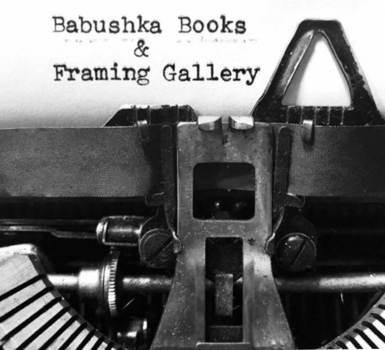 Puede incluir: Una imagen en blanco y negro de una m&aacute;quina de escribir vintage con el texto "Babushka Books & Framing Gallery" escrito en la p&aacute;gina.
