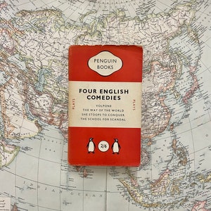 May include: A red Penguin Books paperback with the title "Four English Comedies" and the price "2/6". The book features a list of plays: "Volpone", "The Way of the World", "She Stoops to Conquer", and "The School for Scandal".
