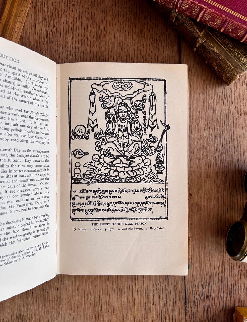 May include: A black and white illustration of a person sitting in a meditative pose. The person is surrounded by clouds and other symbolic imagery. The image is labeled "The Effigy of the Dead Person" and includes a list of items: Mirror, a Couch, Lyre, Vase with flowers, Holy Cake.