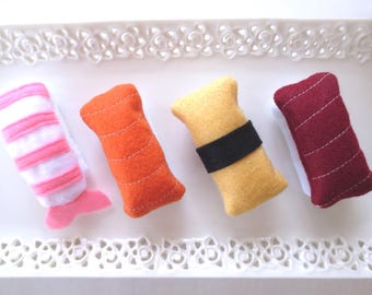 Könnte beinhalten: Vier Sushi-Stücke aus Filz, die in einer Reihe angeordnet sind. Das erste ist eine rosa-weiß gestreifte Garnele, das zweite ist orange, das dritte ist gelb mit einem schwarzen Band und das vierte ist dunkelrot. Jedes Stück hat sichtbare weiße Nähte.
