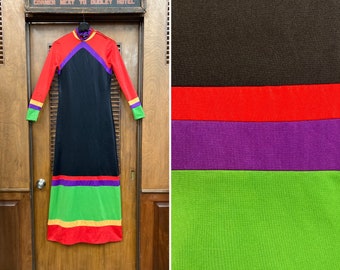 Pode incluir: Um vestido longo preto com gola alta e mangas compridas. O vestido tem um padrão geométrico em vermelho, roxo, verde e amarelo na parte inferior.