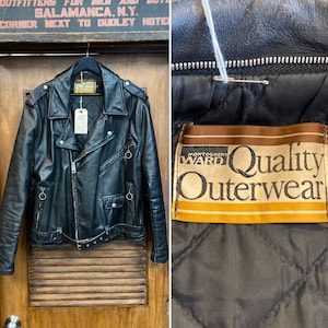 May include: Black leather motorcycle jacket with a classic asymmetrical zipper design, featuring a notched collar, shoulder epaulets, and multiple pockets. The jacket has a belt at the waist and the label reads "Quality Outerwear".