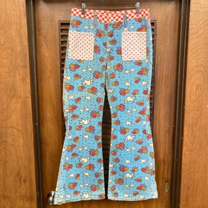 May include: Blue bell bottom pants with a white, red, and orange dove and balloon pattern. The pants have red and white checkered waistband and two pink polka dot pockets.