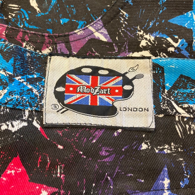 May include: A white tag with a black and red Union Jack flag and the text "ModZart" in a white circle. The tag also has a paint palette design and the text "LONDON" in black.