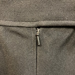 Puede incluir: Primer plano de una cremallera negra en una prenda. La cremallera es de metal y tiene un acabado plateado.