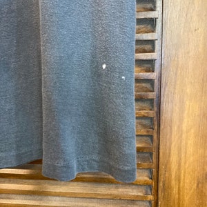 May include: A close-up of a dark gray t-shirt with a slightly faded appearance. The t-shirt is made of a soft, comfortable fabric and has a slightly distressed look.