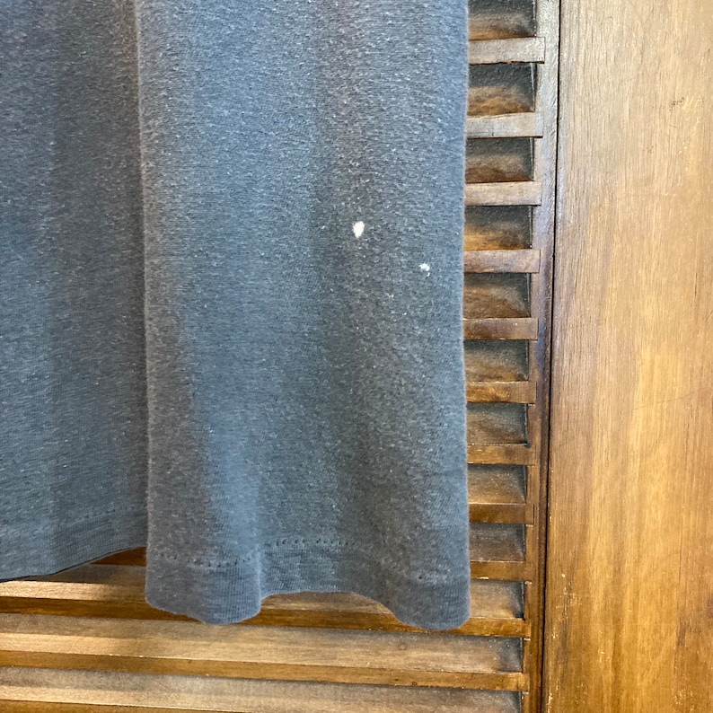 May include: A close-up of a dark gray t-shirt with a slightly faded appearance. The t-shirt is made of a soft, comfortable fabric and has a slightly distressed look.