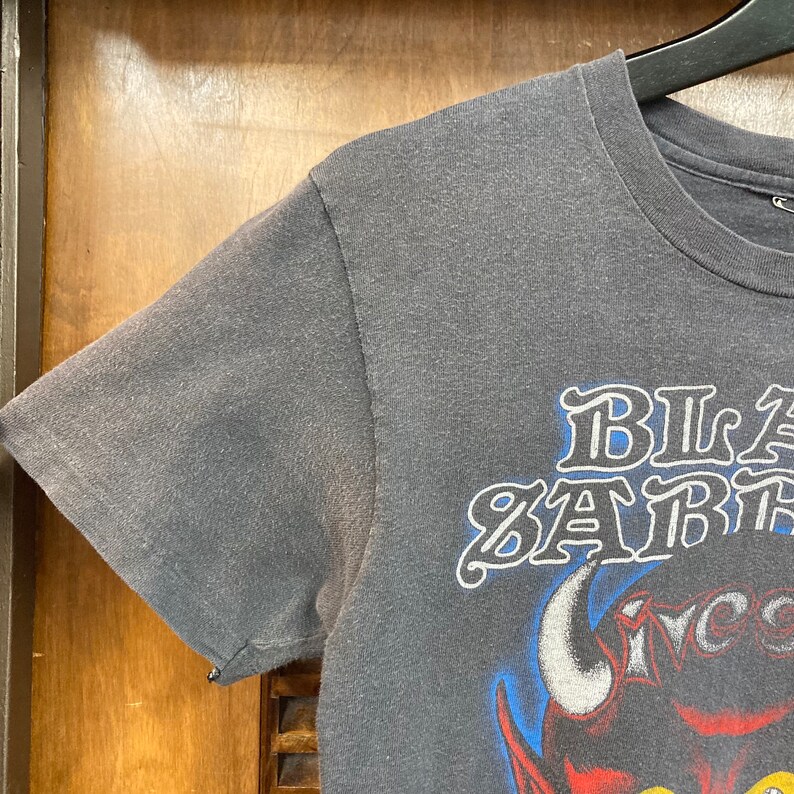 May include: A gray t-shirt with a black and white graphic of a red devil with horns and the text "Black Sabbath" in a white outline.