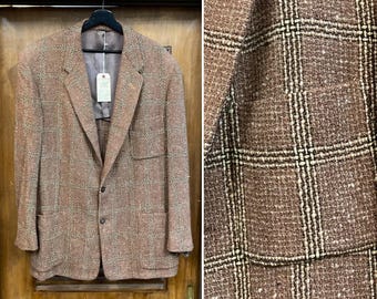 May include: A brown and tan checked blazer with a two-button fastening, hanging on a black hanger. The jacket features two front pockets and a tag. The blazer is made of a textured fabric.