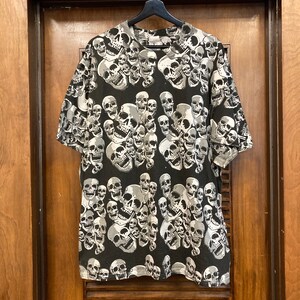 Puede incluir: Camiseta negra con un estampado de calaveras blancas. Las calaveras est&aacute;n dispuestas de forma ca&oacute;tica y superpuestas.