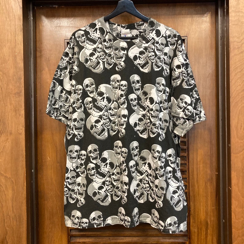 Puede incluir: Camiseta negra con un estampado de calaveras blancas. Las calaveras est&aacute;n dispuestas de forma ca&oacute;tica y superpuestas.