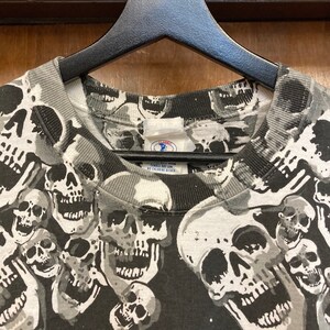 Puede incluir: Camiseta de color negro y blanco con estampado de calaveras y una etiqueta que dice "Cl&aacute;sico, Tejido fino, Lavar a m&aacute;quina con agua fr&iacute;a, Sin cloro".