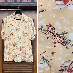 May include: A vintage short-sleeved button-down shirt in a light yellow color, featuring a repeating pattern of cowboys, cacti, and other desert-themed imagery in red, green, and brown. The shirt has a classic collar and two front pockets.