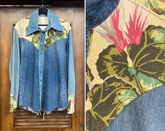 May include: A blue denim shirt with floral fabric panels on the shoulders, yoke, and cuffs. The floral fabric is a beige background with green leaves and pink flowers.