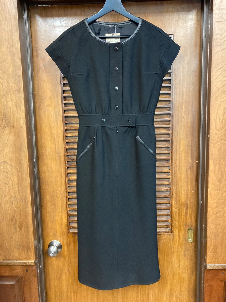 Puede incluir: Un vestido midi negro con cuello redondo, mangas cortas y cintur&oacute;n. El vestido tiene cierre de botones en la parte delantera y un ribete de cuero.