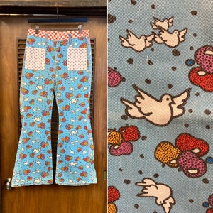 May include: A pair of blue bell bottom jeans with a white dove and colorful balloon pattern. The jeans have red and white checkered waistband and red and white polka dot pockets.