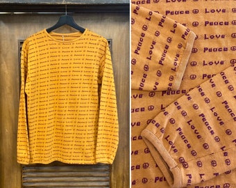 May include: A long-sleeved shirt with a mustard yellow background and a repeating pattern of peace signs and the words "Peace" and "Love" in purple.