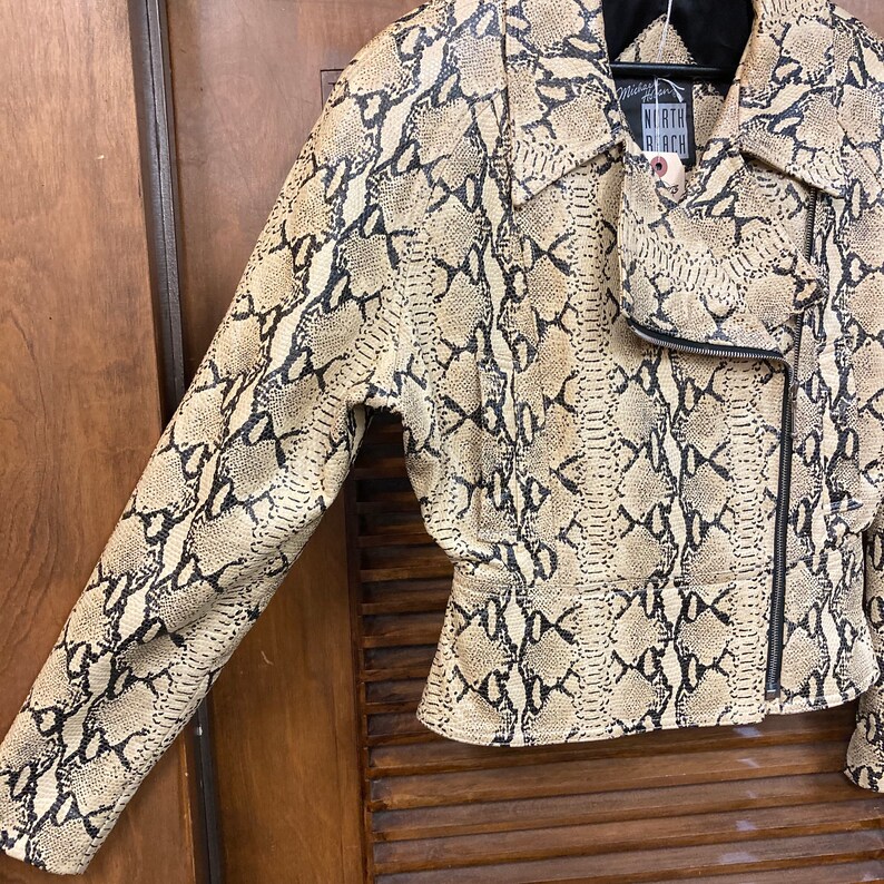 Puede incluir: Una chaqueta de cuero marr&oacute;n y negro con estampado de piel de serpiente y cierre de cremallera. La chaqueta tiene una etiqueta de North Black en el cuello.
