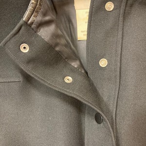 Puede incluir: Chaqueta negra con cuello de cuero y cierres a presi&oacute;n. La chaqueta tiene la etiqueta Courr&egrave;ges Paris en la parte delantera.