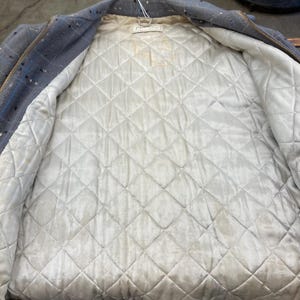 May include: A blue denim jacket with a white quilted lining. The jacket has a zip closure and a white tag on the inside.