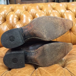 K&ouml;nnte beinhalten: Ein Paar braune Cowboy-Stiefel aus Leder mit einer abgenutzten Ledersohle und einem sternf&ouml;rmigen Design an der Ferse.