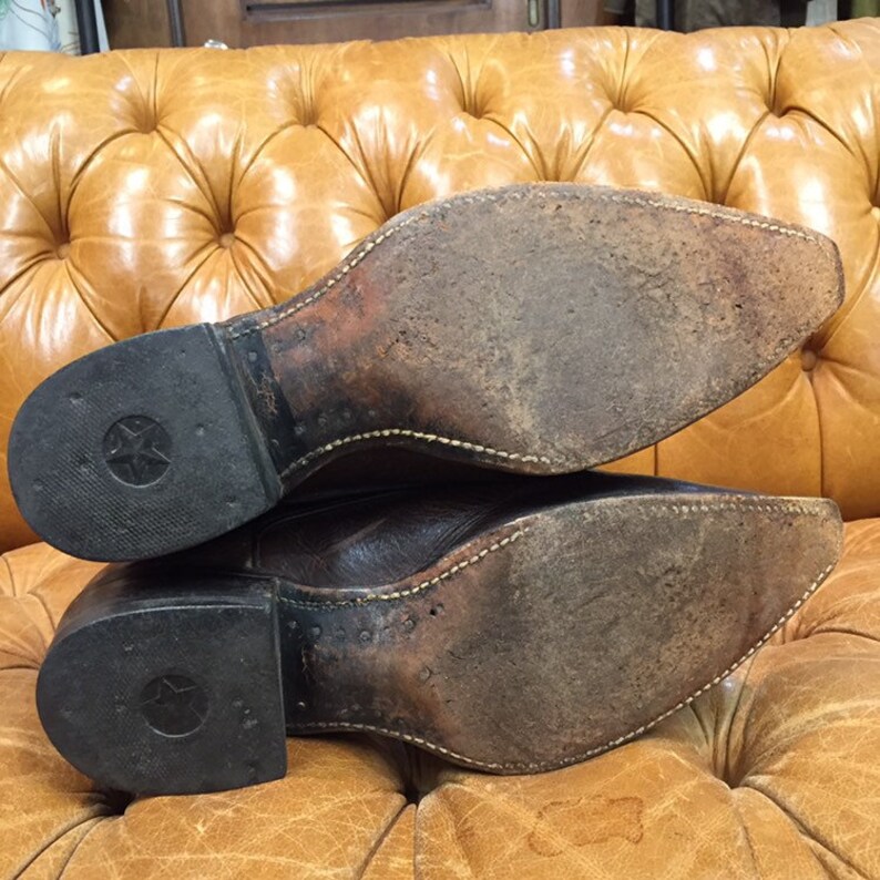 K&ouml;nnte beinhalten: Ein Paar braune Cowboy-Stiefel aus Leder mit einer abgenutzten Ledersohle und einem sternf&ouml;rmigen Design an der Ferse.