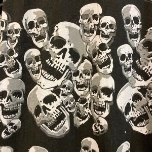 Puede incluir: Patr&oacute;n de calaveras en blanco y negro sobre una tela oscura. Las calaveras son de diferentes tama&ntilde;os y formas, y algunas est&aacute;n sonriendo.