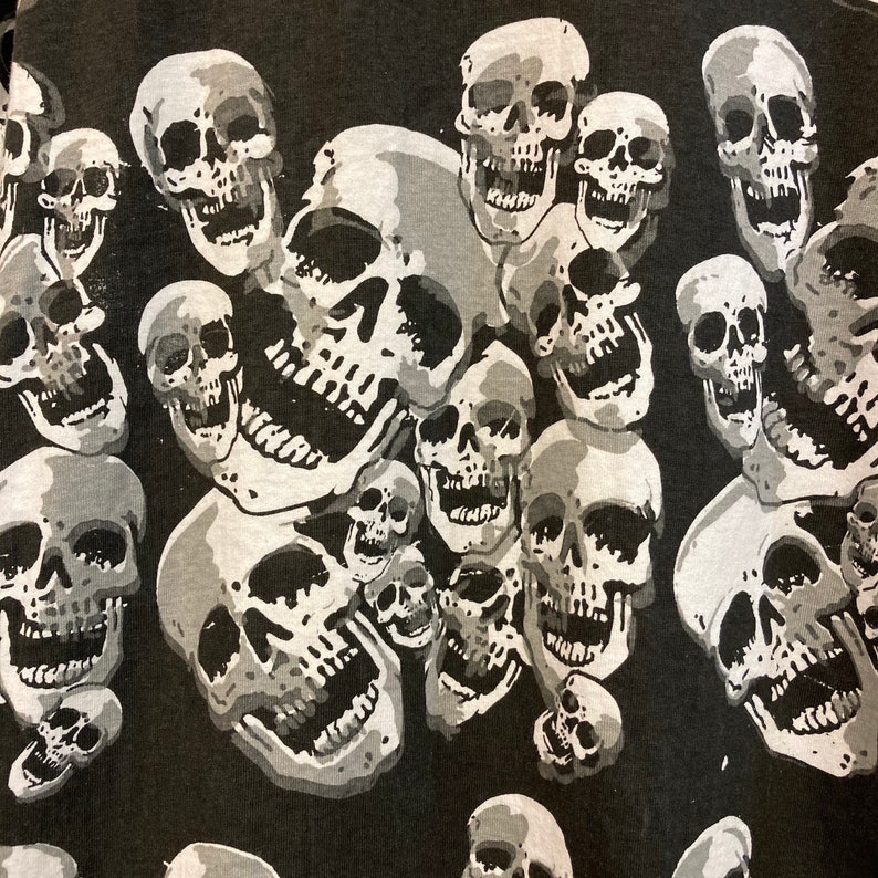 Puede incluir: Patr&oacute;n de calaveras en blanco y negro sobre una tela oscura. Las calaveras son de diferentes tama&ntilde;os y formas, y algunas est&aacute;n sonriendo.