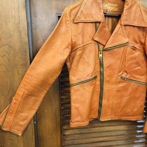 May include: A brown leather jacket with a zipper closure and multiple pockets. The jacket has a collar and long sleeves.