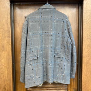 May include: A grey plaid jacket with blue and white accents. The jacket has two pockets on the front and a button closure.