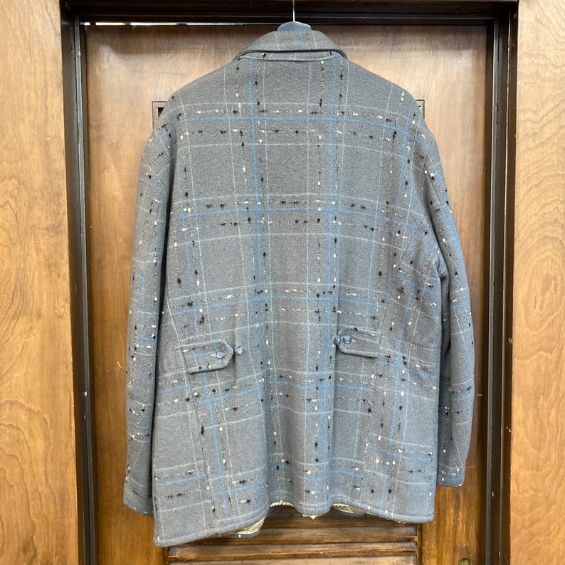 May include: A grey plaid jacket with blue and white accents. The jacket has two pockets on the front and a button closure.