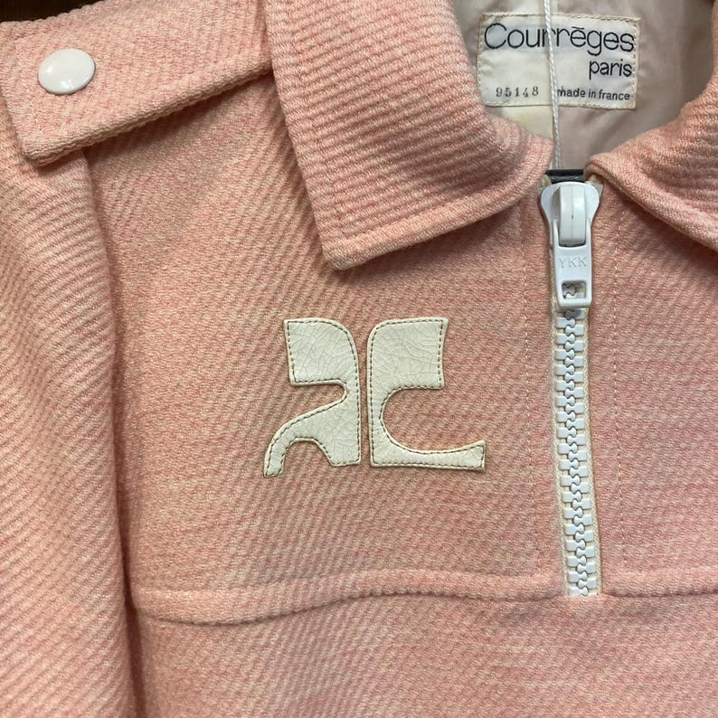 May include: A pink zippered jacket with a white logo that says "AC" and a white zipper. The jacket has a white tag that says "Courr&egrave;ges Paris 95148 made in France".