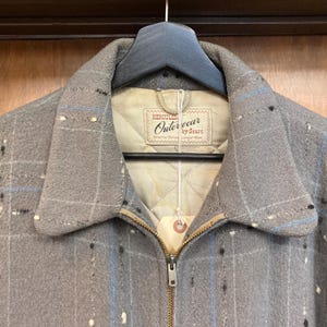 May include: A grey plaid jacket with a zip fastening and a label that reads "Hercules Outerwear by Sears Smarter Styling Longer Wear".