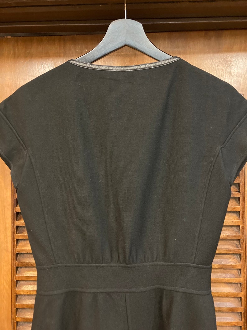 Puede incluir: Un vestido negro de manga corta con un ribete negro alrededor del escote. El vestido tiene un corpi&ntilde;o ajustado y una falda ligeramente acampanada.