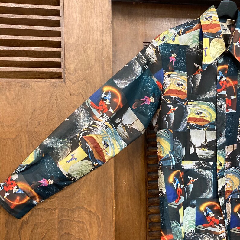 May include: A long-sleeved button-up shirt with a black background and a colorful pattern of cartoon characters and scenes. The characters are in a variety of poses, including flying, swimming, and riding in boats. The scenes are set in a variety of locations, including the ocean, the sky, and a forest.