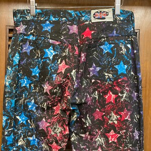 May include: Blue, pink, and white star print jeans with a black background. The jeans have a small patch on the back pocket that says "The Raggedy" and "London".