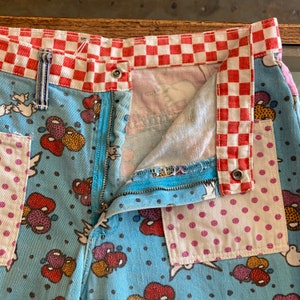 May include: Blue denim shorts with a red and white checkered waistband and a variety of colorful patches. The shorts have a zipper closure and a button fly.
