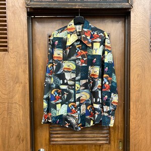 May include: A black long-sleeved button-up shirt with a colorful print of a cartoon character. The print features a variety of scenes and images, including a ship, a wave, and a star.