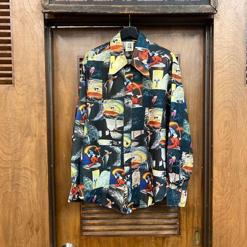 May include: A black long-sleeved button-up shirt with a colorful print of a cartoon character. The print features a variety of scenes and images, including a ship, a wave, and a star.