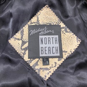 Puede incluir: Una etiqueta negra y beige con el texto "Michael Hoban" y "North Beach" en blanco. La etiqueta est&aacute; unida a una tela beige con un patr&oacute;n de piel de serpiente. La etiqueta tambi&eacute;n tiene el tama&ntilde;o "7/8" impreso en ella.