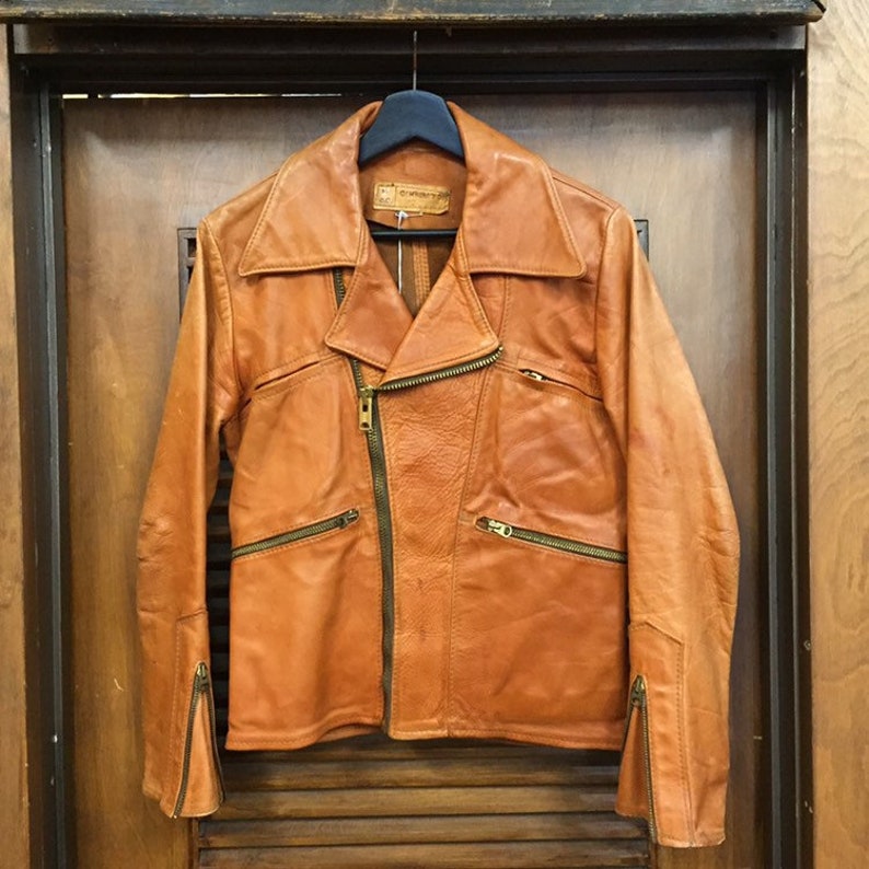 May include: A brown leather motorcycle jacket with a zipper closure and multiple pockets. The jacket has a collar and long sleeves.
