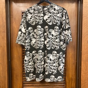 Puede incluir: Camiseta negra con un patr&oacute;n repetido de calaveras blancas.
