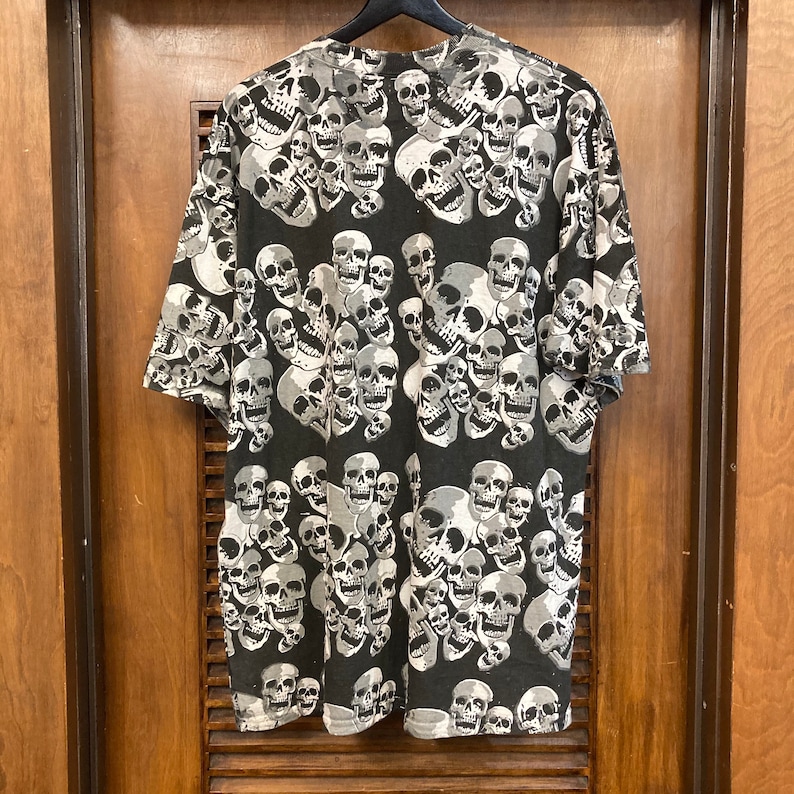 Puede incluir: Camiseta negra con un patr&oacute;n repetido de calaveras blancas.