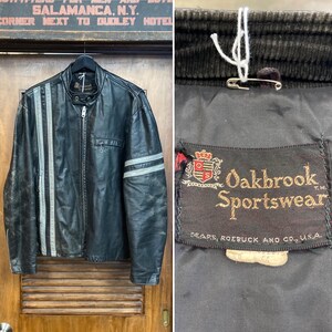 May include: Black leather jacket with silver stripes. The jacket has a zip and a small chest pocket. The label reads "Oakbrook Sportswear" and "SEARS, ROEBUCK AND CO., U.S.A."