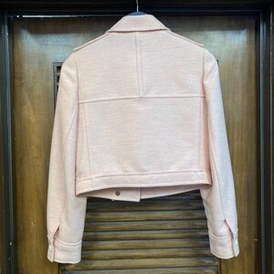 May include: A pink cropped jacket with a zipper closure and long sleeves. The jacket has a textured fabric and a slightly oversized fit.