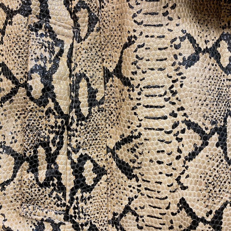 Puede incluir: Primer plano de una tela con estampado de piel de serpiente. La tela es beige con marcas negras.
