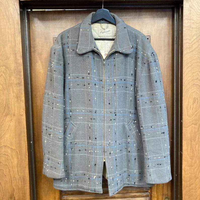 May include: A grey wool jacket with a blue and white checked pattern and black flecks. The jacket has a zip fastening and two pockets. The label on the jacket reads "Abercrombie & Fitch".